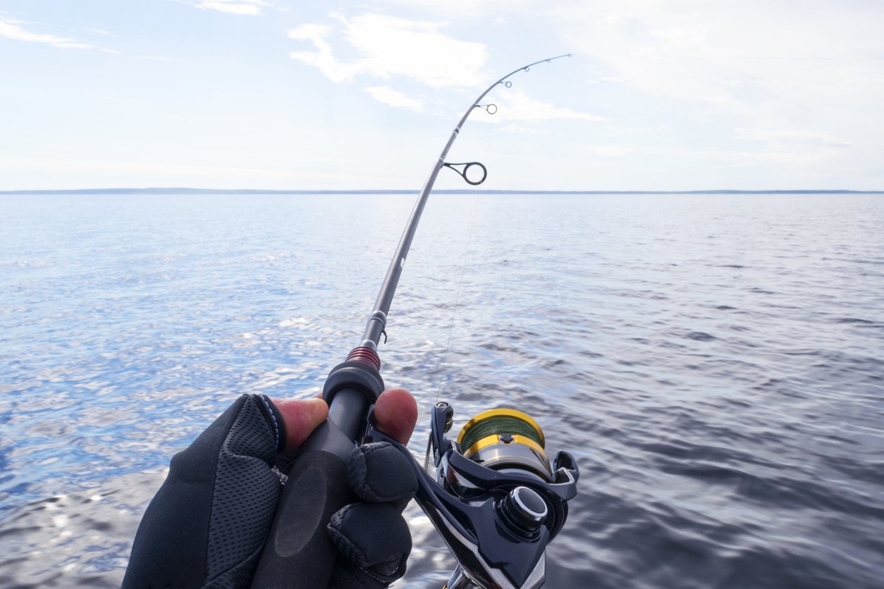hand-with-glove-holding-fishing-rod-with-line-in-ocean-water